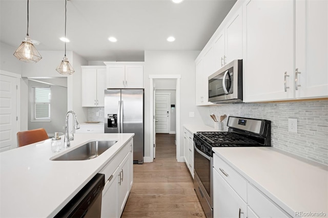 kitchen featuring white cabinets, sink, hanging light fixtures, light hardwood / wood-style floors, and stainless steel appliances