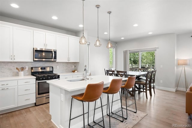 kitchen featuring a center island with sink, white cabinets, light wood-type flooring, and appliances with stainless steel finishes