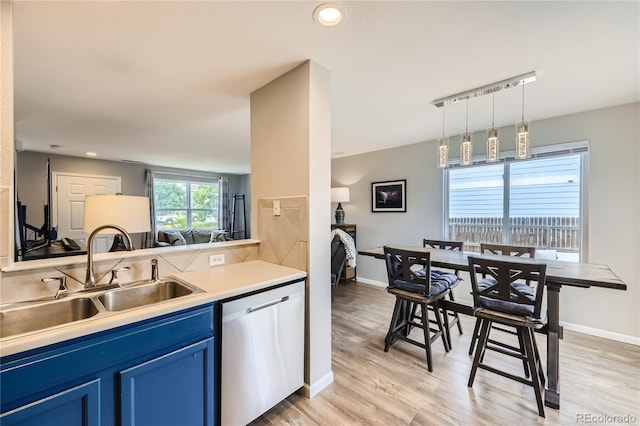 kitchen with dishwasher, sink, hanging light fixtures, blue cabinetry, and light hardwood / wood-style flooring