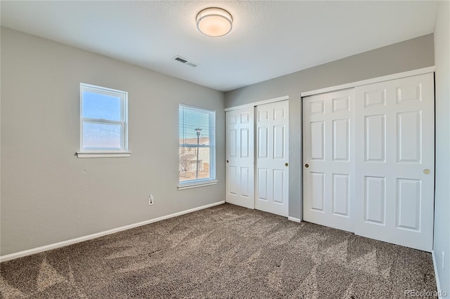 unfurnished bedroom featuring dark colored carpet, two closets, and a textured ceiling