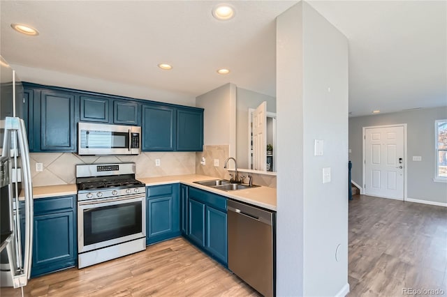 kitchen featuring sink, light hardwood / wood-style flooring, blue cabinetry, stainless steel appliances, and tasteful backsplash