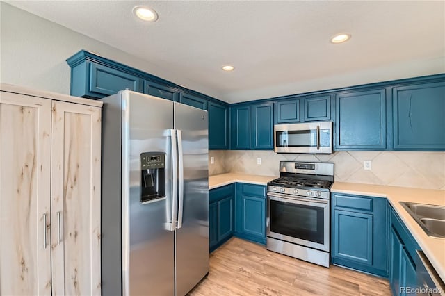 kitchen with stainless steel appliances, tasteful backsplash, blue cabinets, and light wood-type flooring