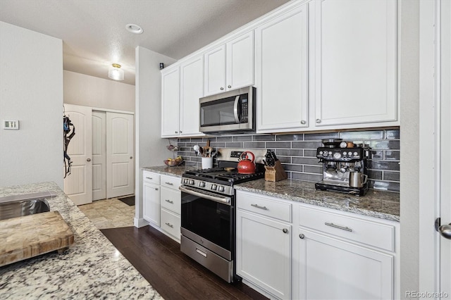 6834 Clay St N, Denver, CO 80221 - kitchen with appliances with stainless steel finishes, white cabinetry, light stone counters, tasteful backsplash, and dark wood-style floors