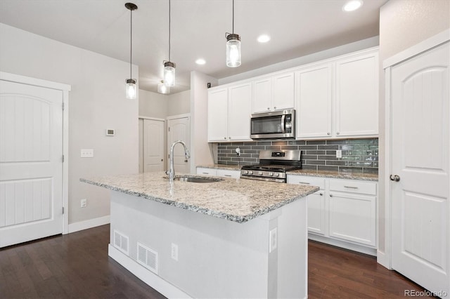 6834 Clay St N, Denver, CO 80221 - kitchen featuring appliances with stainless steel finishes, dark wood-style flooring, tasteful backsplash, an island with sink, and white cabinetry