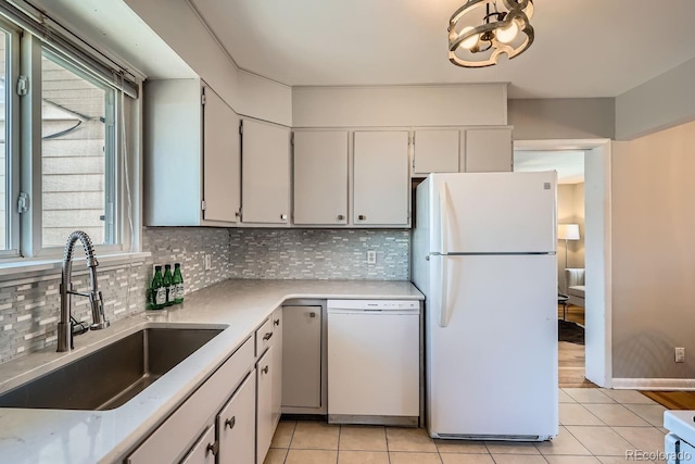 kitchen featuring a sink, tasteful backsplash, white appliances, light countertops, and light tile patterned floors