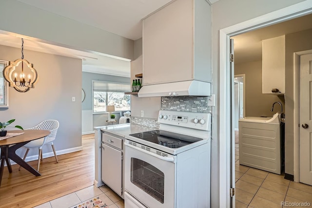 kitchen with white electric range, under cabinet range hood, tasteful backsplash, light tile patterned flooring, and washer / dryer