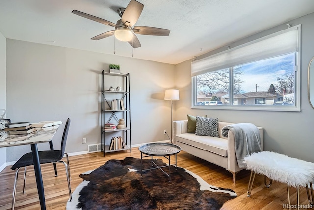 living area featuring visible vents, baseboards, light wood-style floors, and a ceiling fan