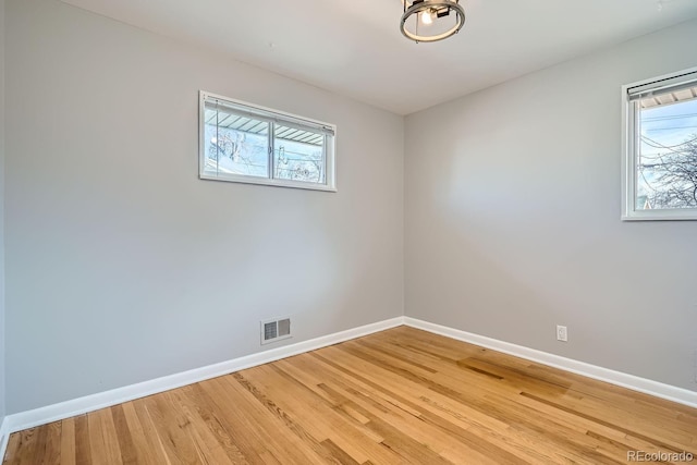 empty room featuring visible vents, plenty of natural light, light wood-style flooring, and baseboards