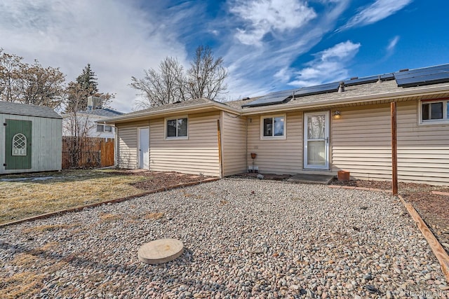 back of property with an outbuilding, a shed, roof mounted solar panels, and fence