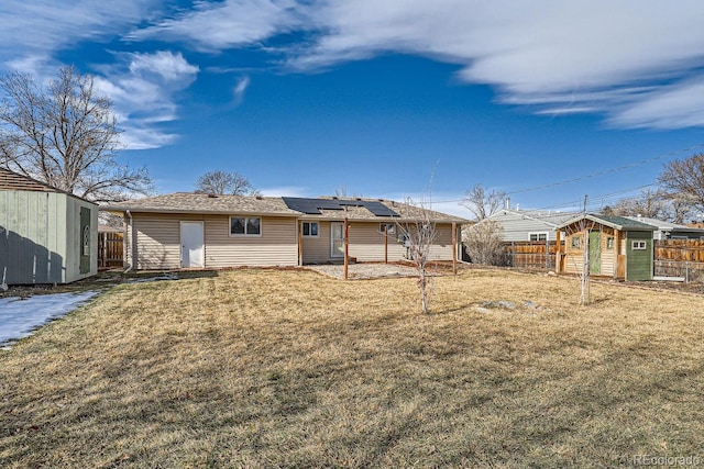 back of property with a storage unit, a lawn, fence, an outdoor structure, and solar panels