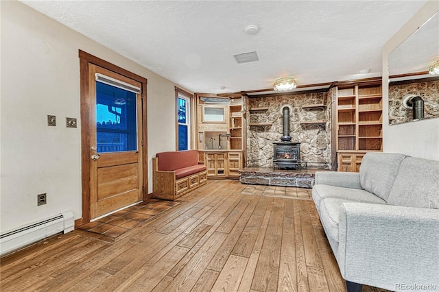 living room with a baseboard radiator, built in shelves, hardwood / wood-style flooring, and a wood stove