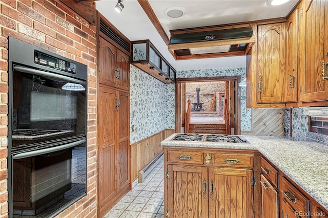 kitchen with tasteful backsplash, stainless steel gas stovetop, light stone counters, black double oven, and brick wall