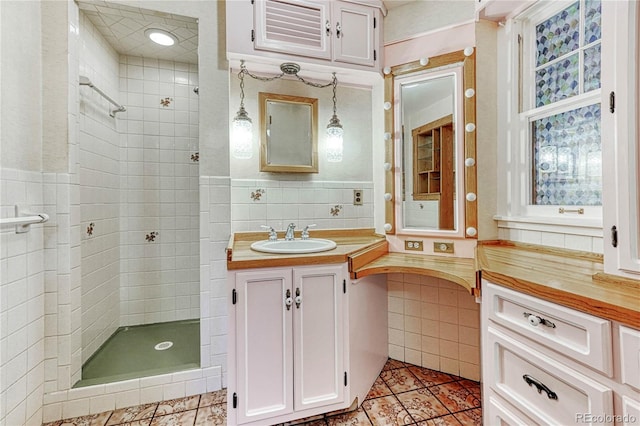 bathroom with vanity, tile patterned floors, tile walls, a tile shower, and backsplash