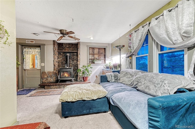 living room with a wood stove, carpet, a textured ceiling, and ceiling fan