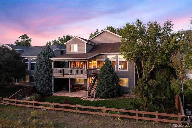 back of house at dusk with a lawn, a patio, stairway, and a fenced front yard