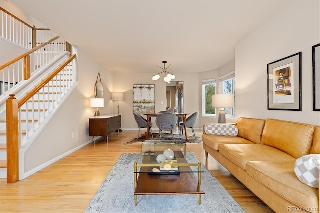 living room featuring an inviting chandelier, stairs, baseboards, and wood finished floors