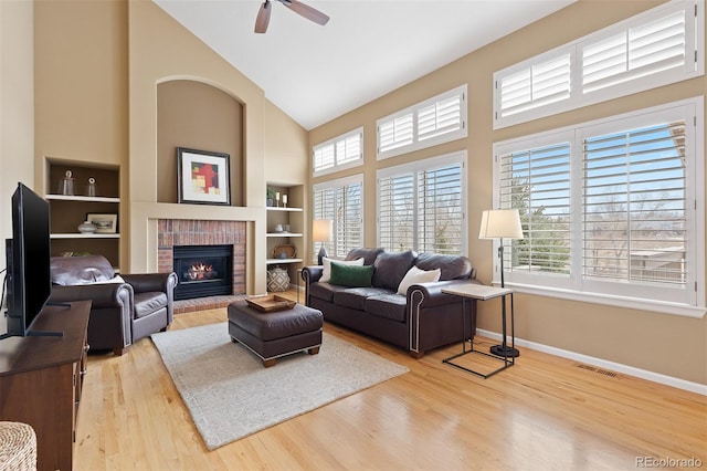 living room with high vaulted ceiling, built in shelves, wood finished floors, baseboards, and a brick fireplace