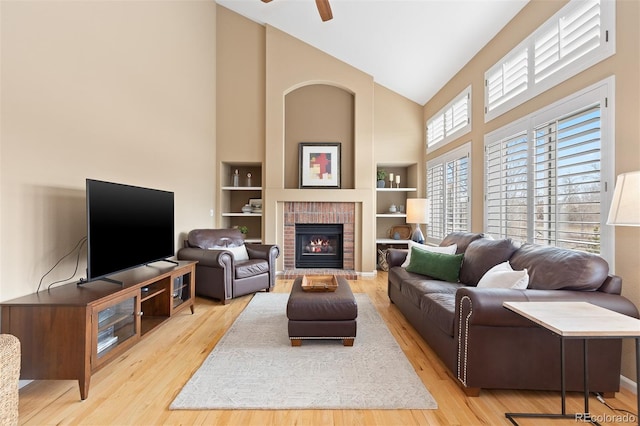 living area with built in shelves, a fireplace, a ceiling fan, wood finished floors, and high vaulted ceiling