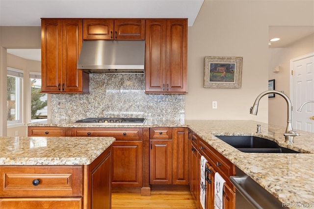 kitchen with tasteful backsplash, light stone counters, extractor fan, stainless steel gas stovetop, and a sink