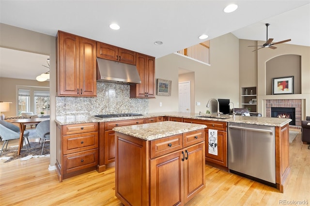 kitchen with under cabinet range hood, a peninsula, open floor plan, appliances with stainless steel finishes, and a brick fireplace