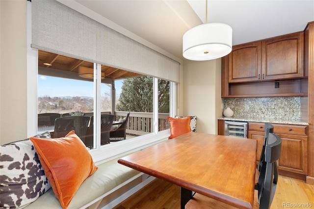 dining room with a bar, wine cooler, light wood-style flooring, and a healthy amount of sunlight