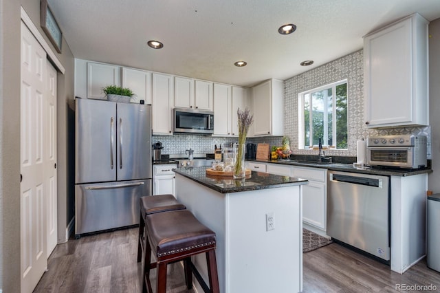 kitchen with appliances with stainless steel finishes, wood finished floors, a sink, and a center island