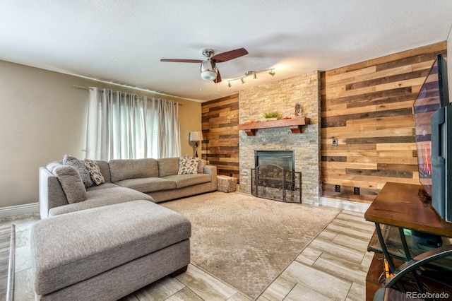 living room with ceiling fan, a textured ceiling, a fireplace, and wooden walls