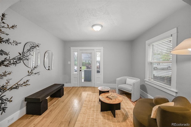 living room with healthy amount of natural light, light wood-style floors, baseboards, and a textured ceiling