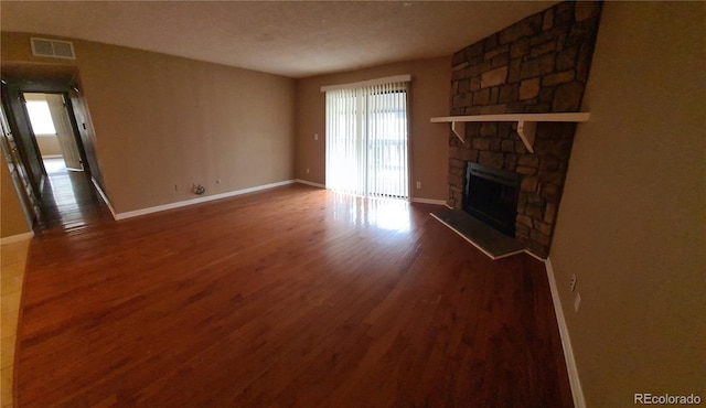 unfurnished living room with visible vents, a fireplace, baseboards, and wood finished floors