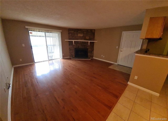 unfurnished living room with a textured ceiling, a stone fireplace, wood finished floors, and baseboards