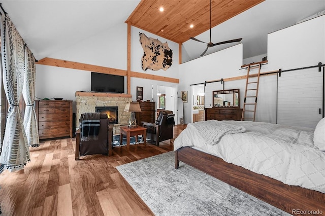 663 Brookside Dr, Bailey, CO 80421 - bedroom with a barn door, wood finished floors, high vaulted ceiling, a stone fireplace, and recessed lighting