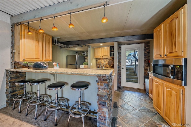 kitchen featuring hanging light fixtures, stainless steel appliances, a peninsula, a kitchen bar, and stone tile flooring