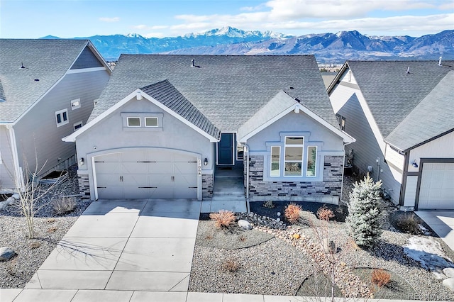 view of front facade with driveway, roof with shingles, stone siding, a garage, and a mountain view