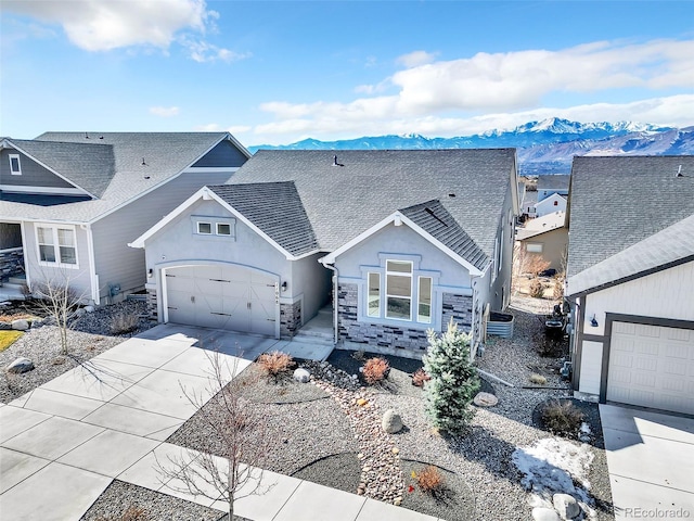 view of front of property with stucco siding, driveway, stone siding, a mountain view, and a shingled roof