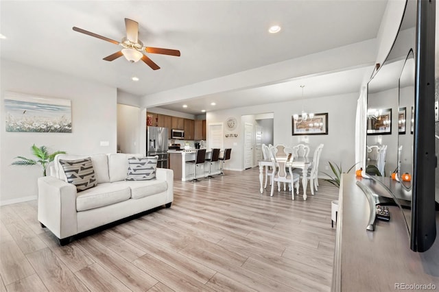 living room with ceiling fan with notable chandelier and light hardwood / wood-style floors