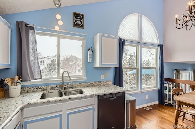 kitchen featuring lofted ceiling, sink, wood-type flooring, black dishwasher, and white cabinets