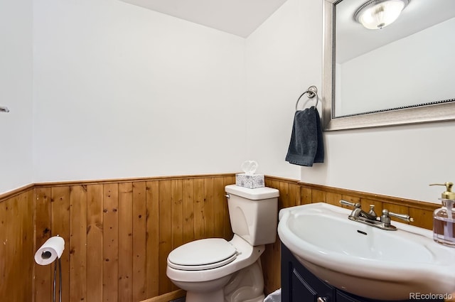 bathroom featuring wooden walls, vanity, and toilet