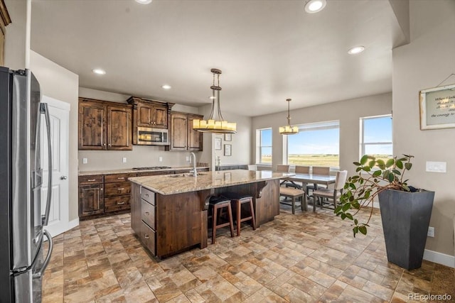 45425 Wolf Creek Dr, Bennett, CO 80102 - kitchen with stainless steel appliances, light stone finish flooring, a kitchen island with sink, a breakfast bar, and plenty of natural light