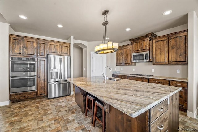 45425 Wolf Creek Dr, Bennett, CO 80102 - kitchen featuring appliances with stainless steel finishes, light stone countertops, arched walkways, a kitchen island with sink, and pendant lighting