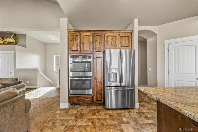 45425 Wolf Creek Dr, Bennett, CO 80102 - kitchen with stainless steel appliances, arched walkways, light stone countertops, open floor plan, and dark stone finish floors
