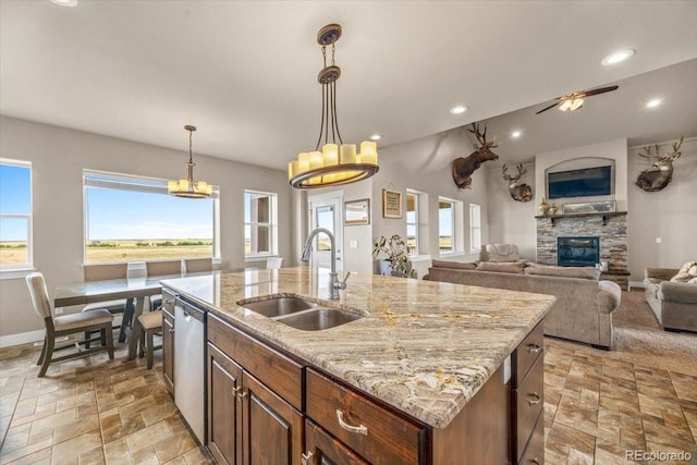 45425 Wolf Creek Dr, Bennett, CO 80102 - kitchen featuring stainless steel dishwasher, light stone finish floors, a stone fireplace, a center island with sink, and open floor plan