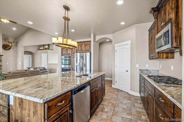 45425 Wolf Creek Dr, Bennett, CO 80102 - kitchen featuring appliances with stainless steel finishes, arched walkways, a large island with sink, light stone counters, and recessed lighting