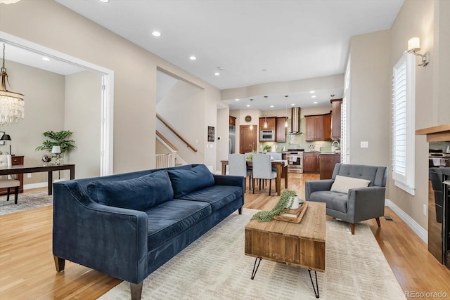 living room featuring light wood finished floors, recessed lighting, a notable chandelier, baseboards, and stairs