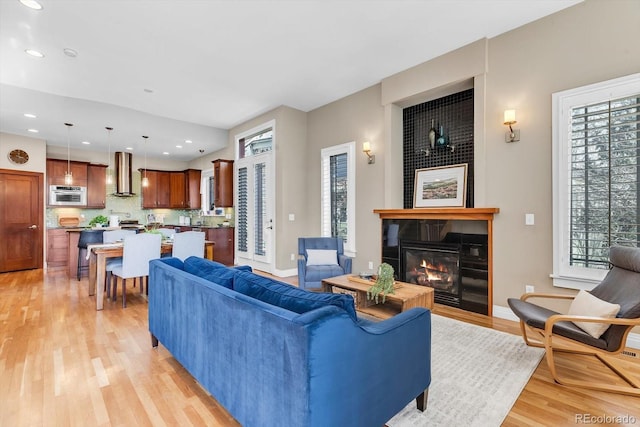 living area featuring recessed lighting, light wood-type flooring, baseboards, and a glass covered fireplace