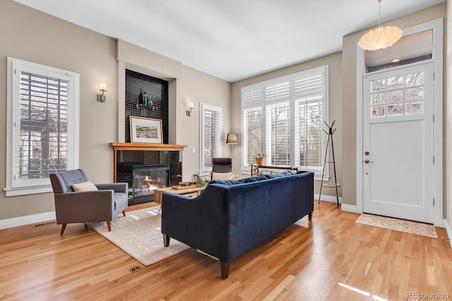 living room featuring baseboards, a tile fireplace, light wood finished floors, and visible vents