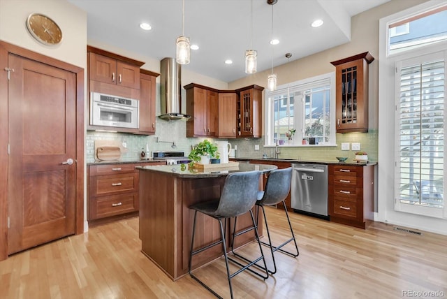 kitchen with appliances with stainless steel finishes, visible vents, a kitchen bar, wall chimney range hood, and light wood-type flooring