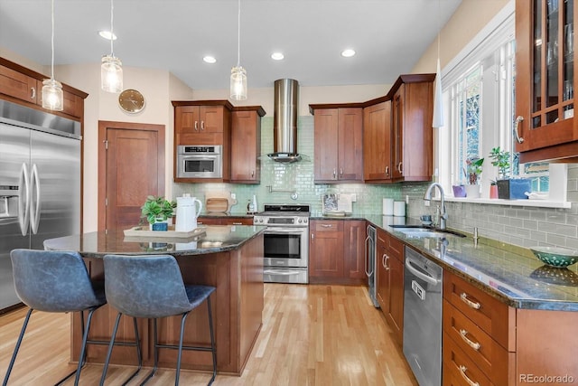 kitchen with a sink, a kitchen bar, wall chimney exhaust hood, light wood-style floors, and stainless steel appliances