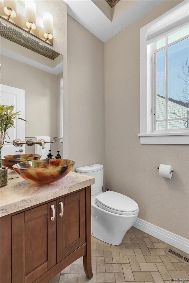 half bath with vanity, toilet, baseboards, and visible vents