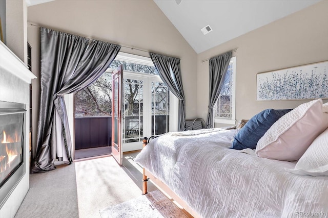carpeted bedroom with access to outside, visible vents, a glass covered fireplace, and high vaulted ceiling
