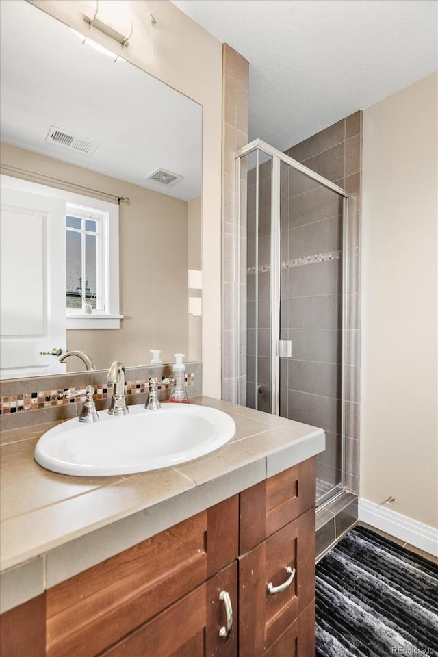 bathroom with a stall shower, vanity, and visible vents